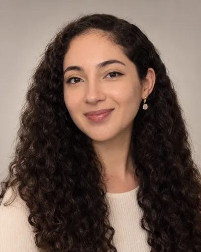 Fiona Roch, smiling, with long curly dark hair, in a cream top against a soft grey studio background